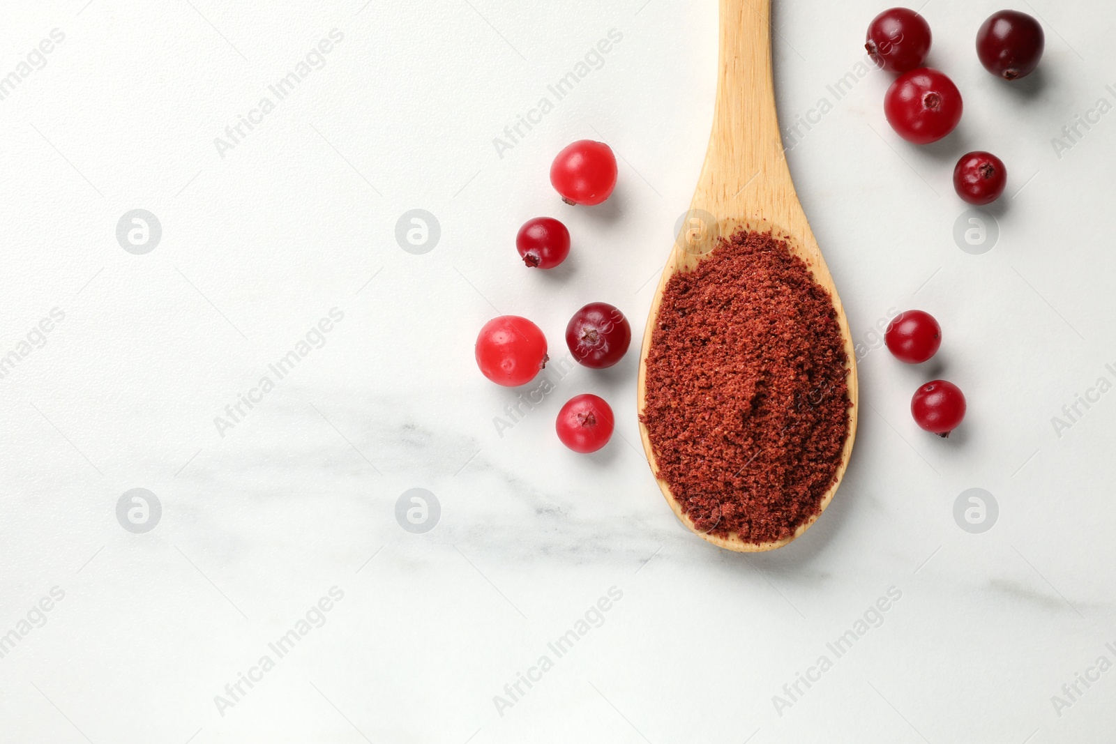 Photo of Dried cranberry powder in spoon and fresh berries on white marble table, top view. Space for text