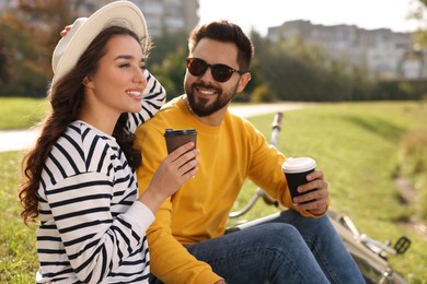 Photo of Beautiful young couple with takeaway coffee spending time together in park