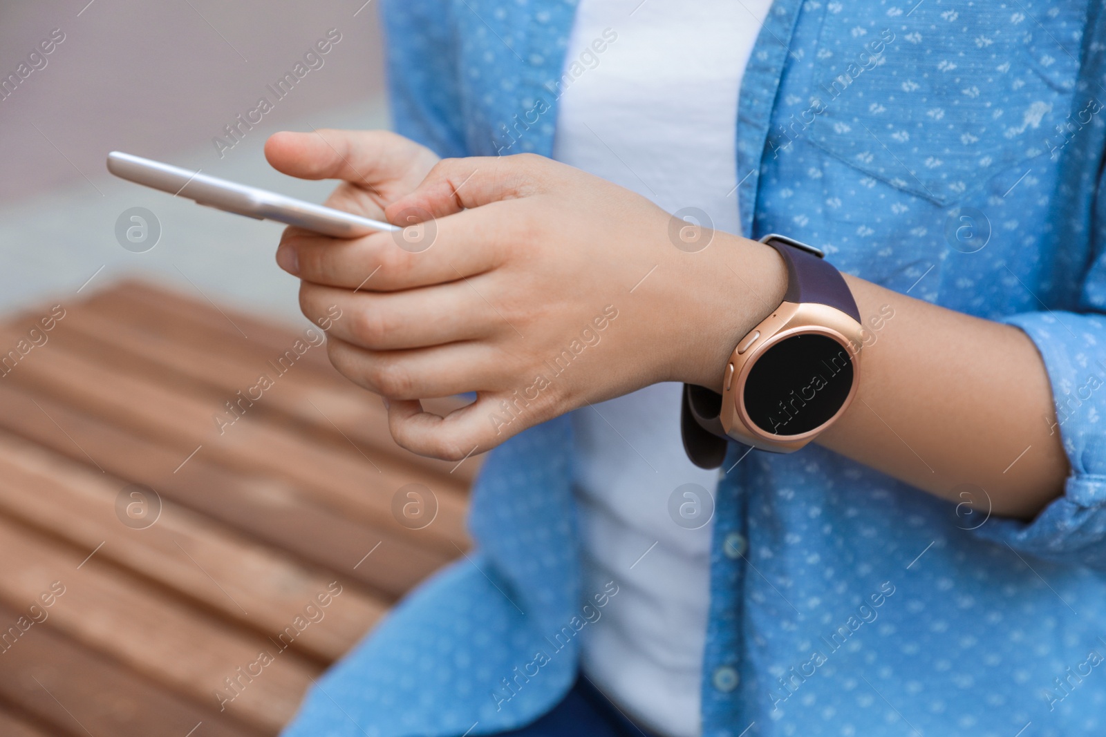 Photo of Woman with modern smart watch using phone outdoors, closeup