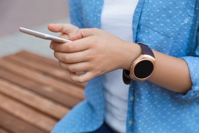 Photo of Woman with modern smart watch using phone outdoors, closeup
