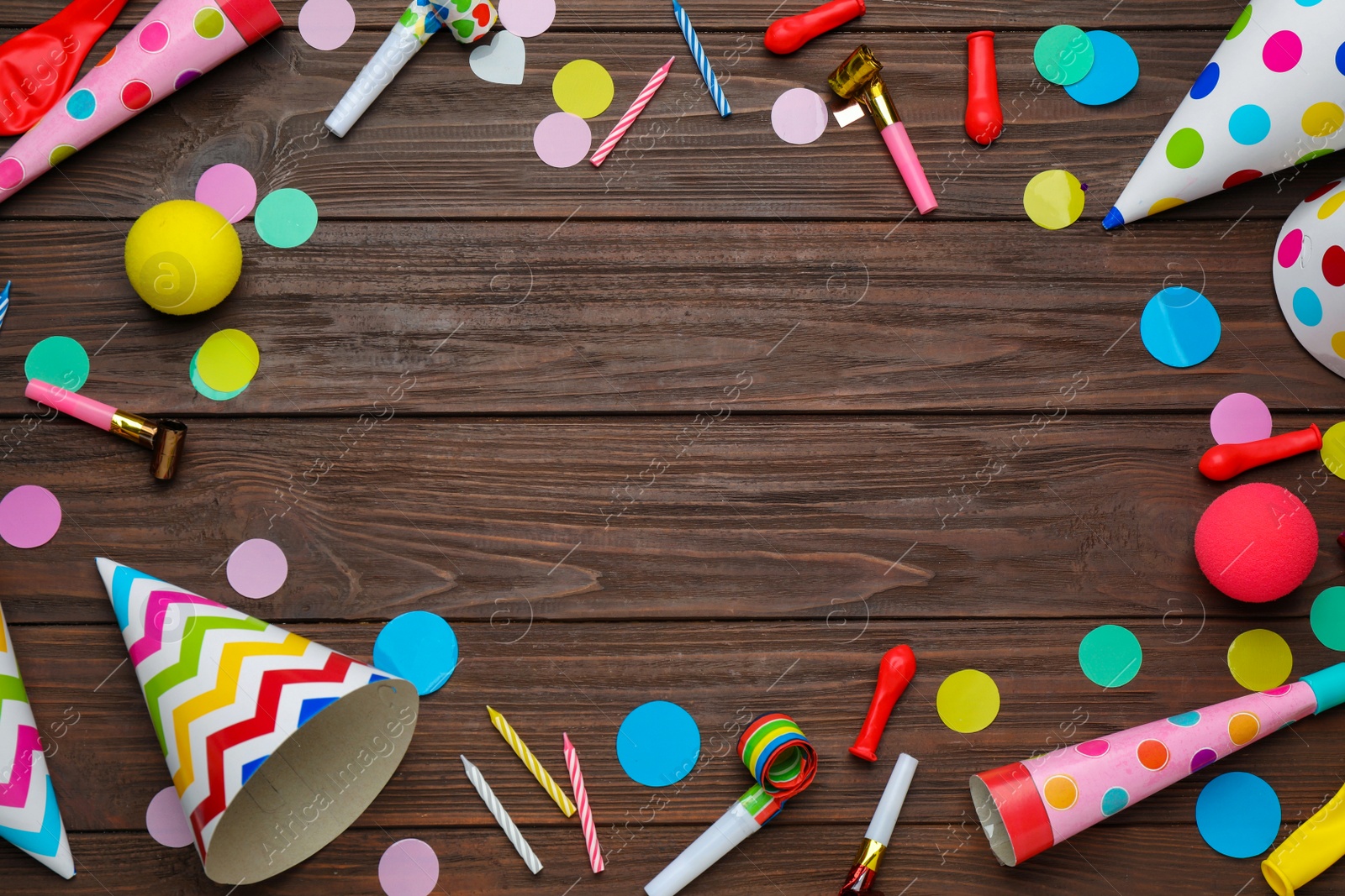 Photo of Frame made of colorful party hats and other festive items on wooden table, flat lay. Space for text