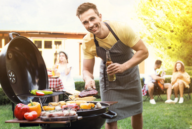 Image of Young man with beer cooking on barbecue grill outdoors