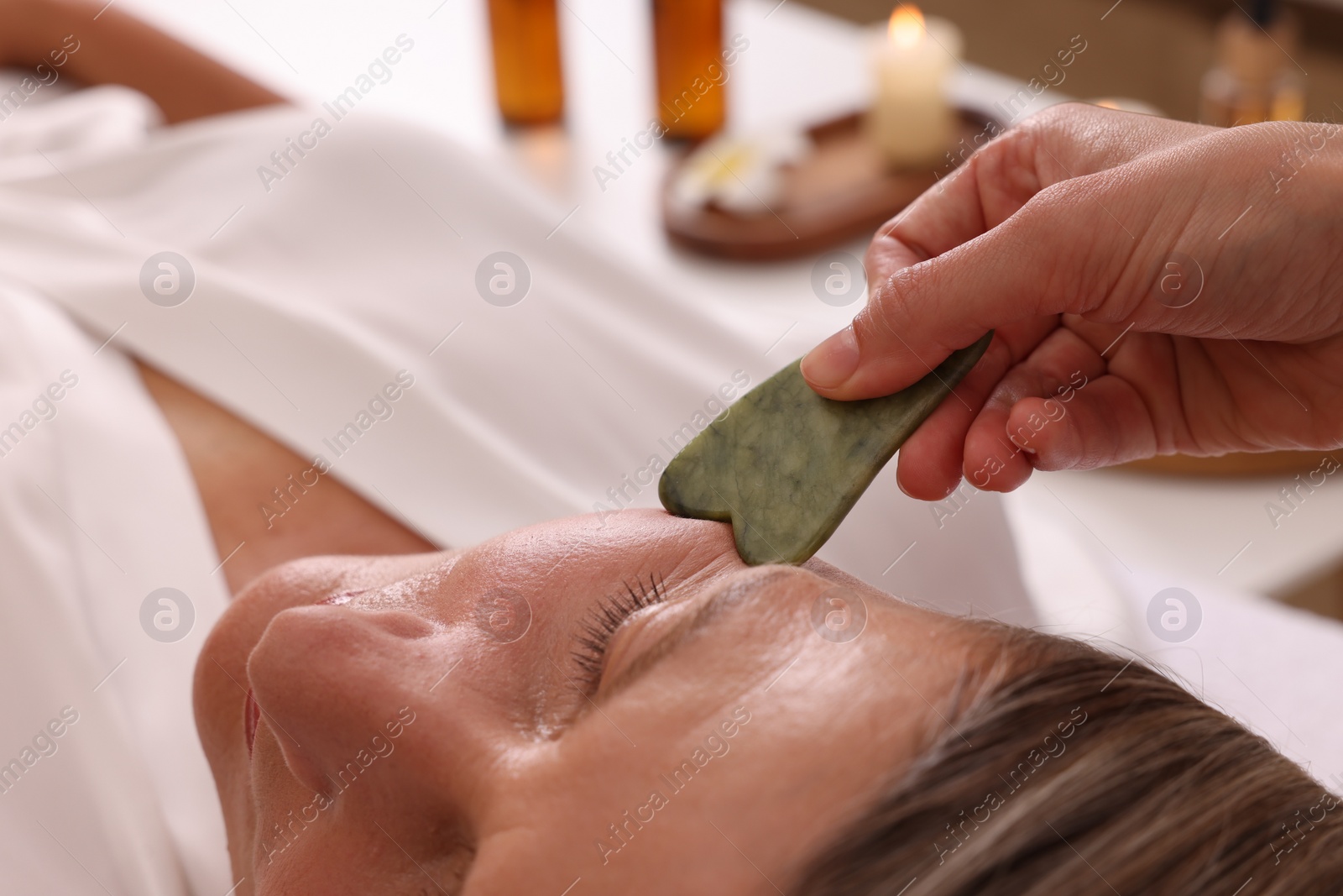 Photo of Woman receiving facial massage with jade gua sha tool in beauty salon, closeup