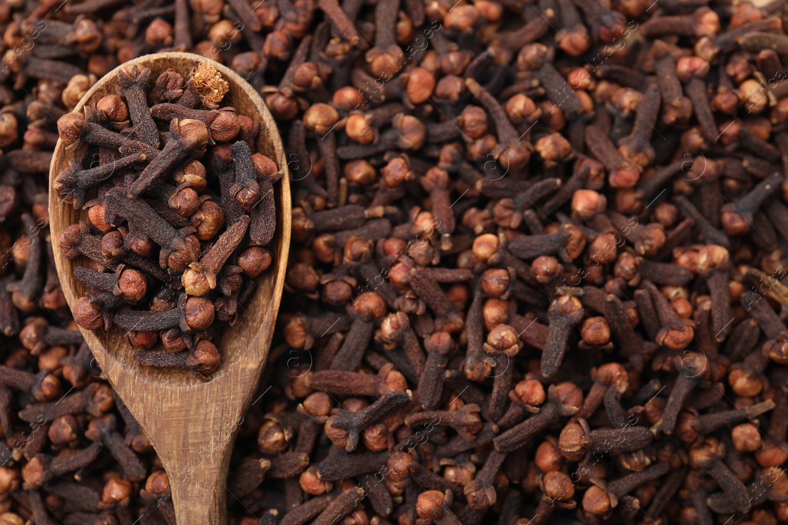 Photo of Many aromatic cloves and wooden spoon as background, top view. Space for text