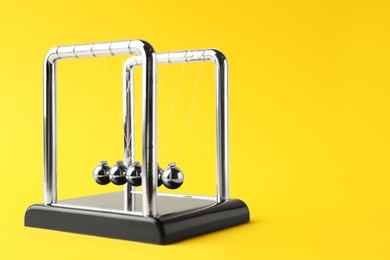 Newton's cradle on yellow background, space for text. Physics law of energy conservation