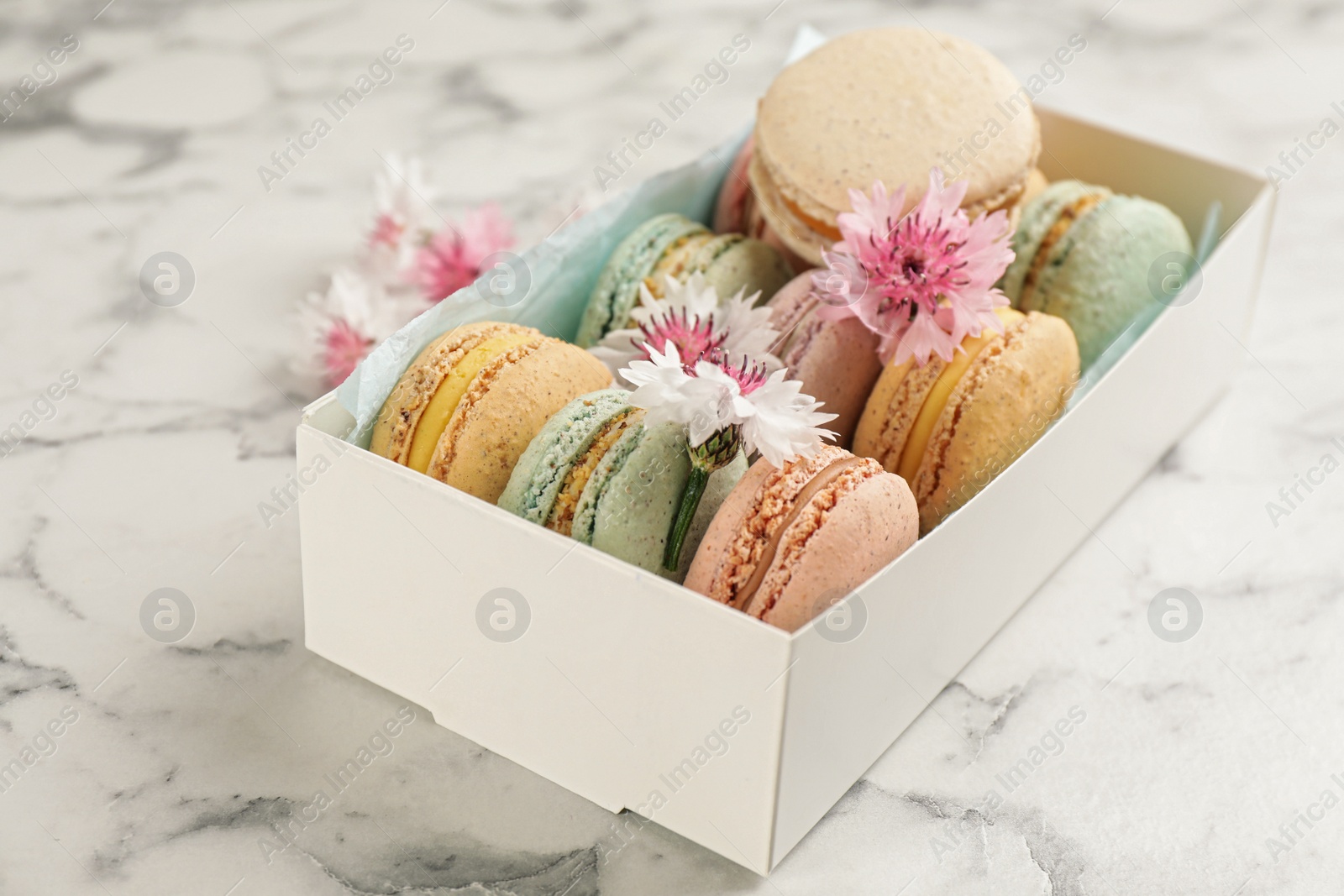 Photo of Delicious macarons and flowers in box on white marble table