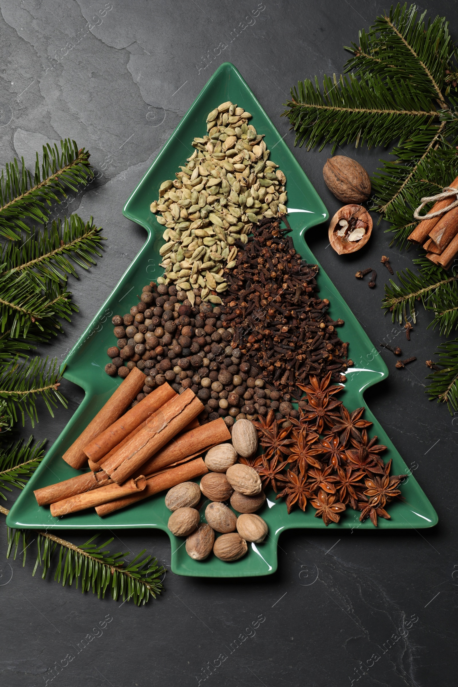 Photo of Different spices, nuts and fir branches on dark gray textured table, flat lay