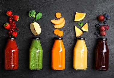 Photo of Flat lay composition with bottles of delicious juices and fresh ingredients on black table