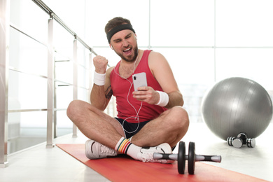 Photo of Lazy young man with sport equipment using smartphone on yoga mat