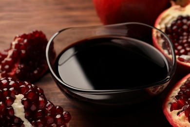 Photo of Glass bowl of tasty pomegranate sauce and fresh ripe fruit on wooden table, closeup