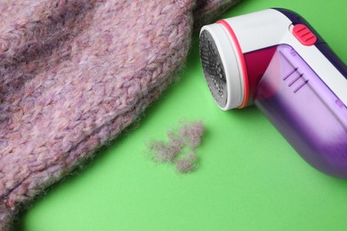 Photo of Modern fabric shaver, lint and woolen sweater on green background