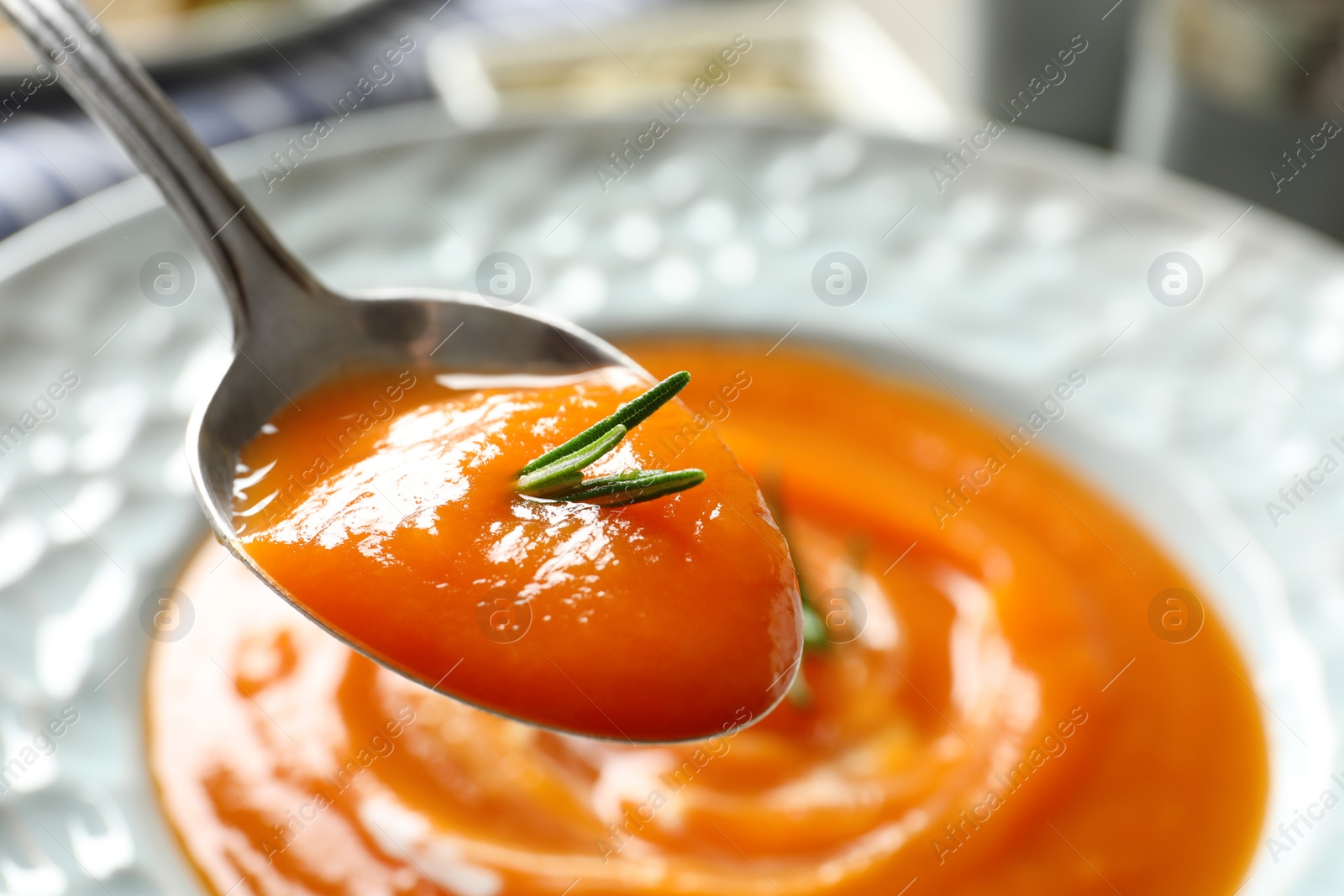 Photo of Spoon of sweet potato soup with rosemary over plate, closeup