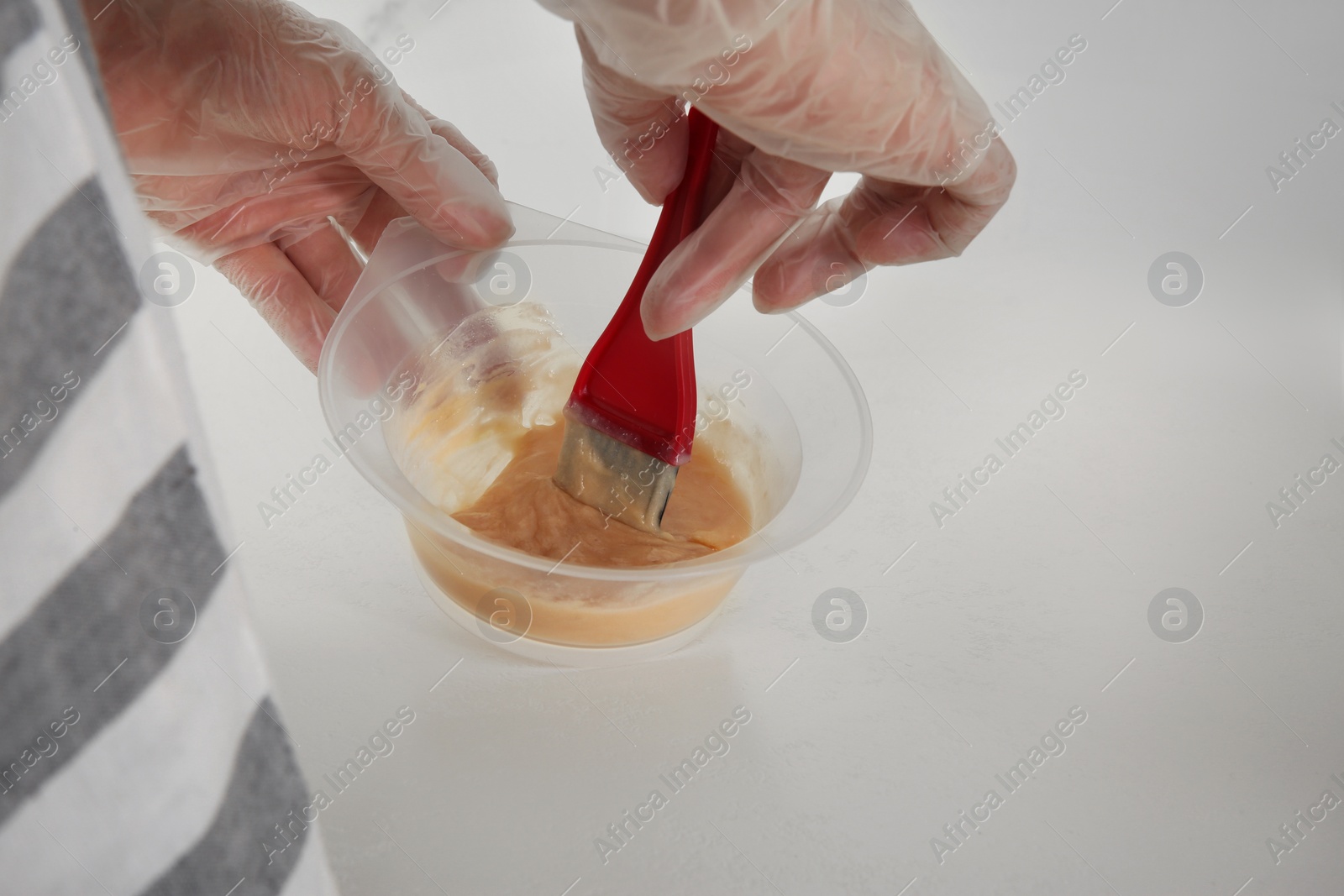 Photo of Woman preparing hair dye in bowl at white table, closeup