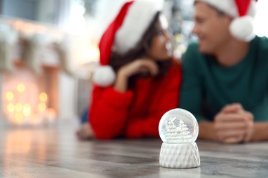 Photo of Happy couple on floor indoors, focus on snow globe