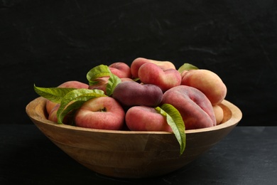 Fresh ripe donut peaches with leaves in bowl on dark table