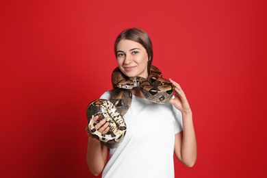 Photo of Young woman with boa constrictor on red background. Exotic pet