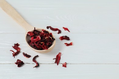 Photo of Hibiscus tea. Spoon with dried roselle calyces on white wooden table. Space for text