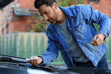 Photo of Man checking motor oil level with dipstick outdoors
