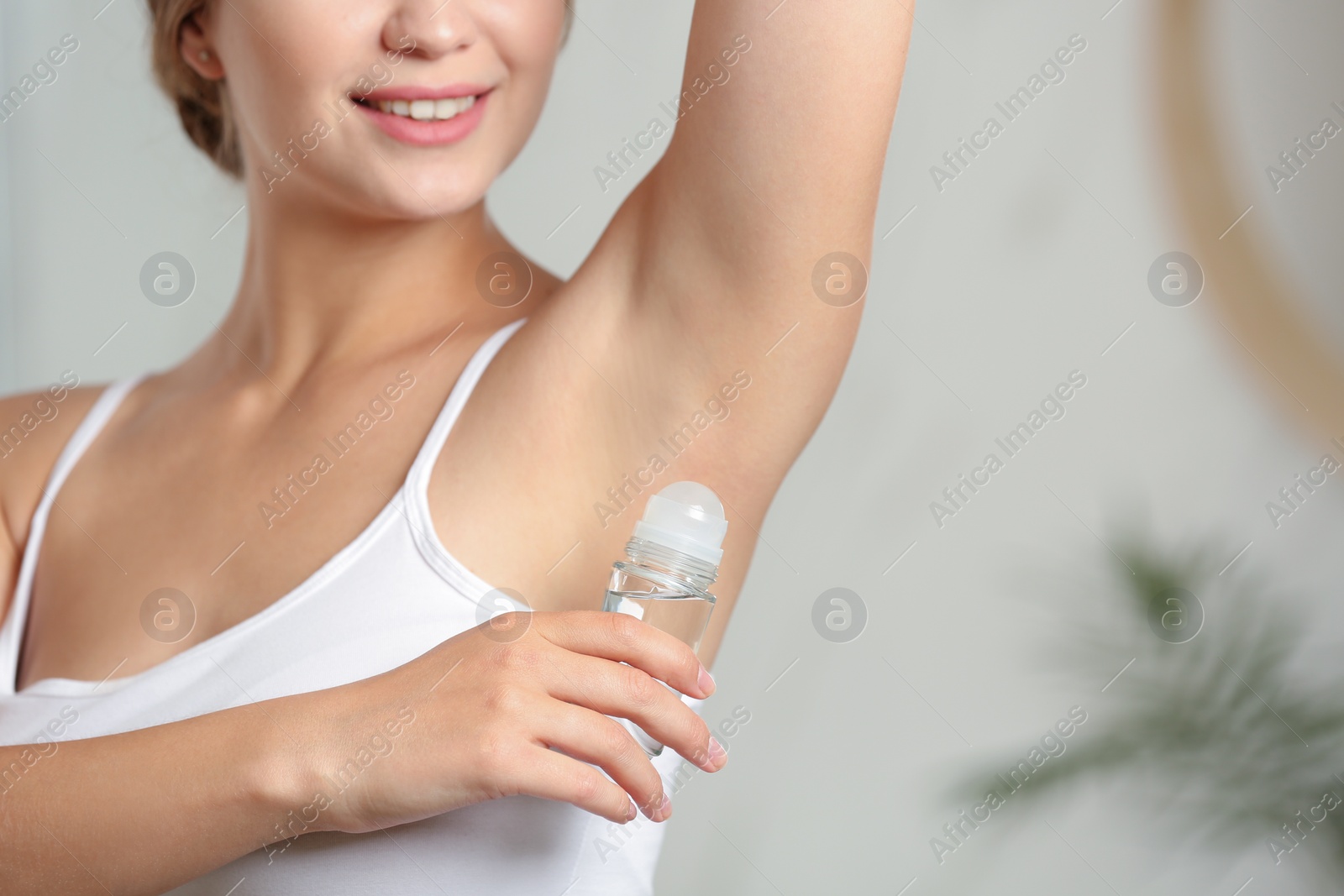 Photo of Young woman applying roll-on deodorant indoors, closeup