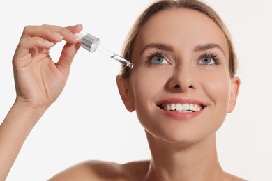 Photo of Beautiful woman applying cosmetic serum onto her face on white background, closeup