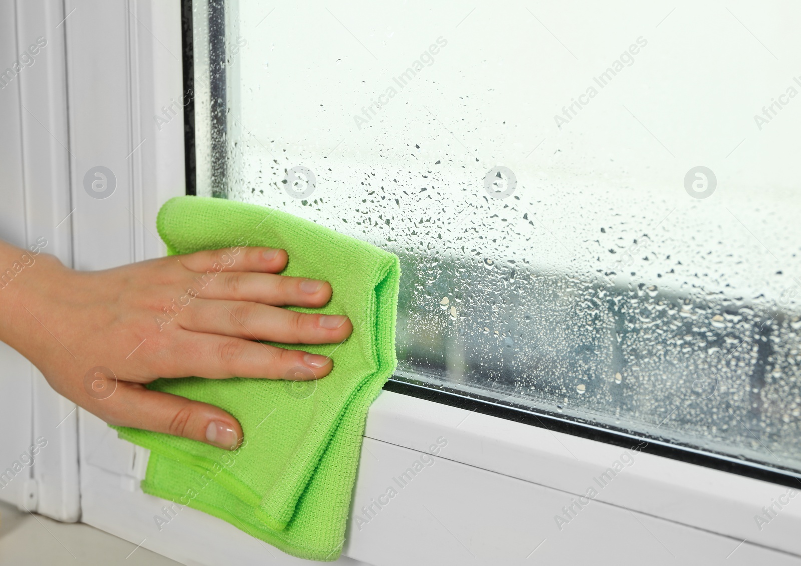 Photo of Woman wiping window glass with drops of condensate indoors, closeup. Space for text