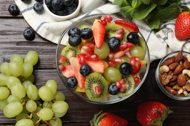 Photo of Tasty fruit salad in bowl and ingredients on wooden table, flat lay