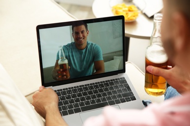 Photo of Friends drinking beer while communicating through online video conference at home. Social distancing during coronavirus pandemic