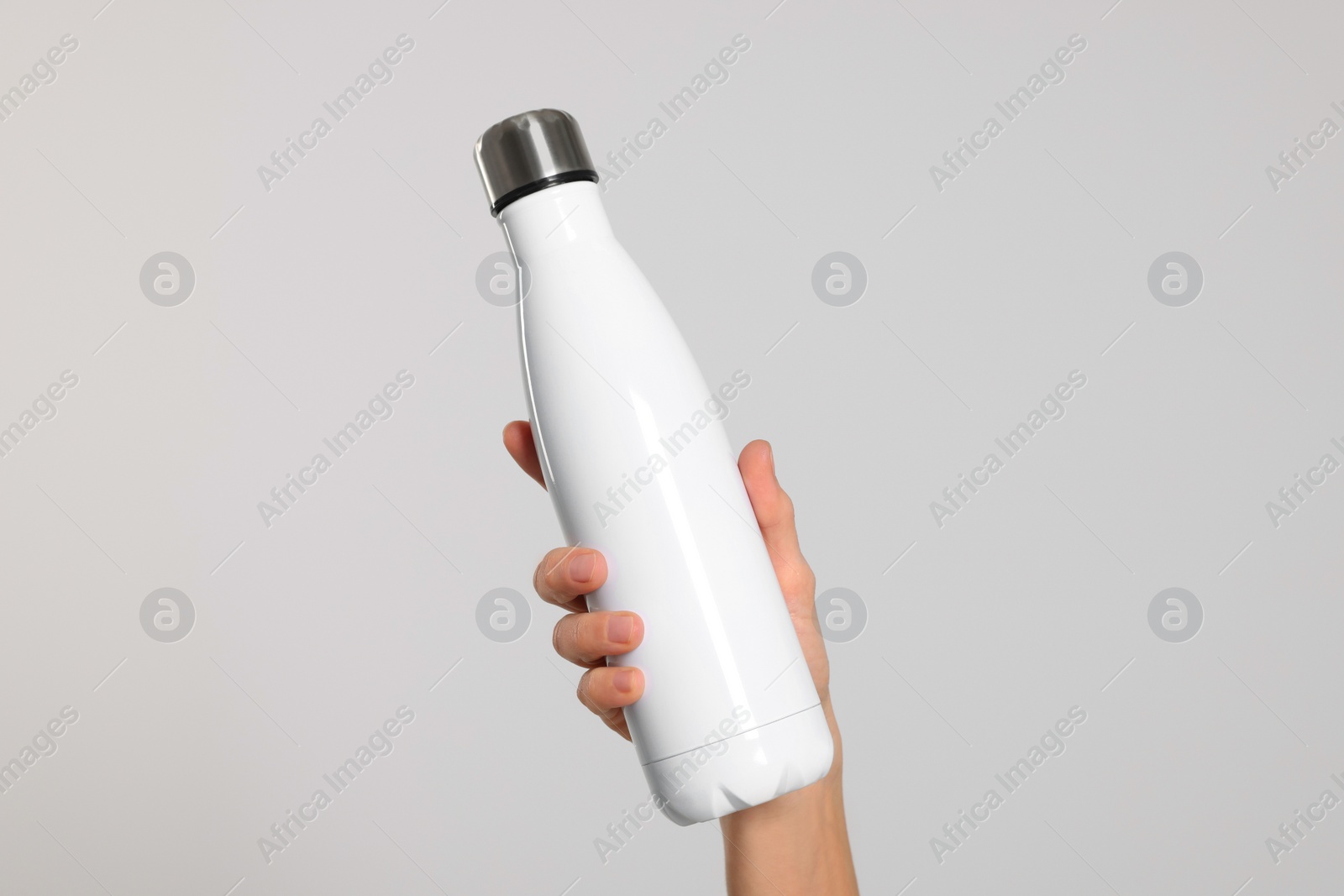 Photo of Woman holding thermo bottle of drink on light background, closeup