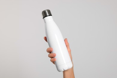 Woman holding thermo bottle of drink on light background, closeup