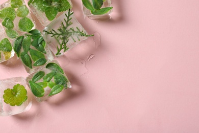 Ice cubes with leaves on pink background, flat lay. Space for text