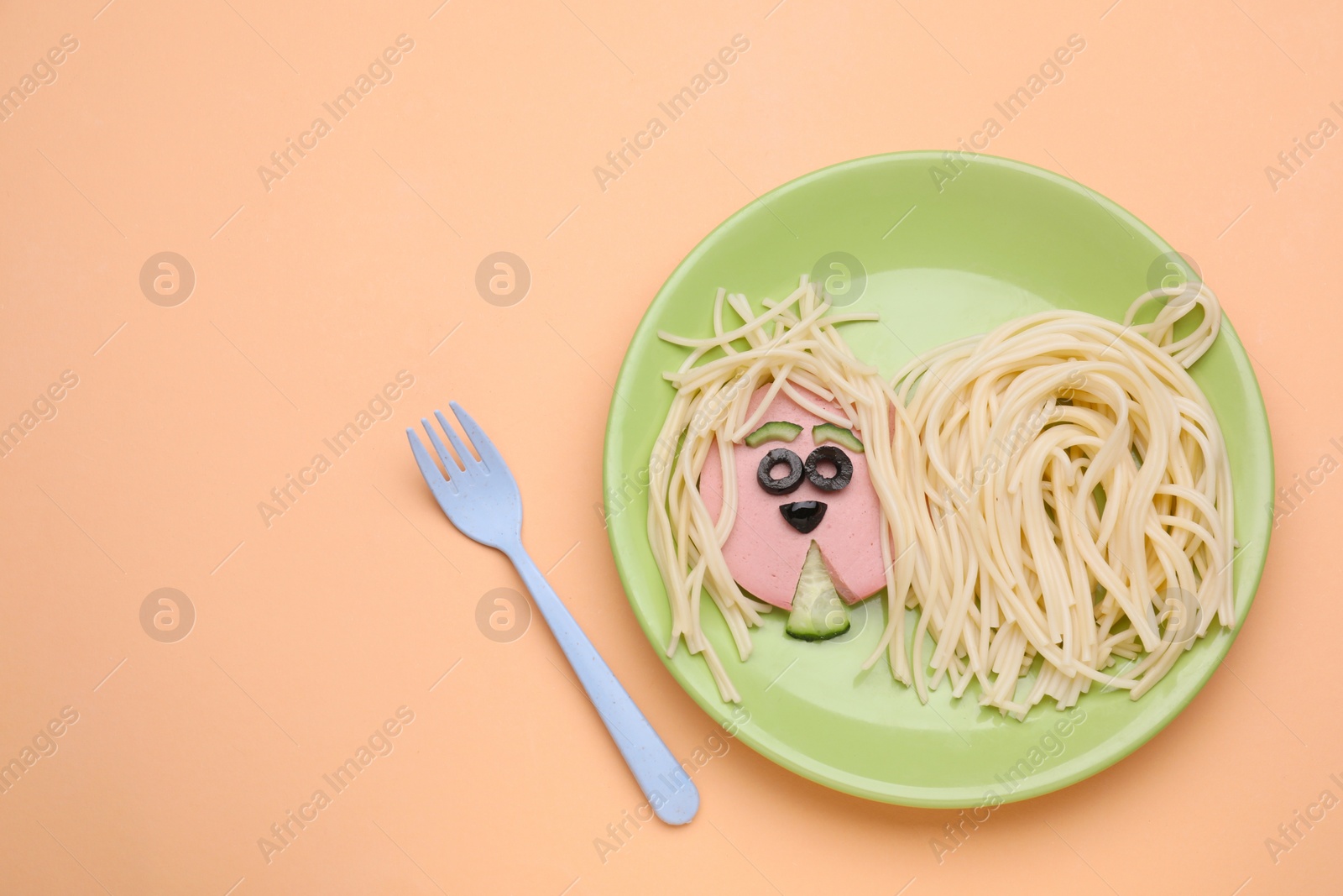 Photo of Creative serving for kids. Plate with cute dog made of tasty pasta, sausage and cucumber on pale orange table, flat lay. Space for text