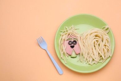 Creative serving for kids. Plate with cute dog made of tasty pasta, sausage and cucumber on pale orange table, flat lay. Space for text