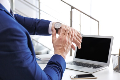 Photo of Young businessman checking time on his wristwatch at workplace. Time management