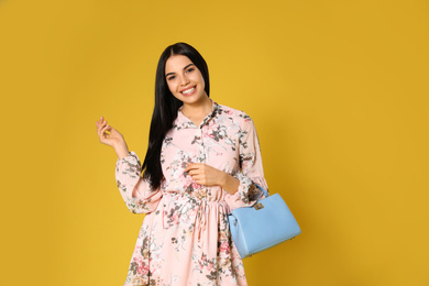 Young woman wearing floral print dress with stylish handbag on yellow background