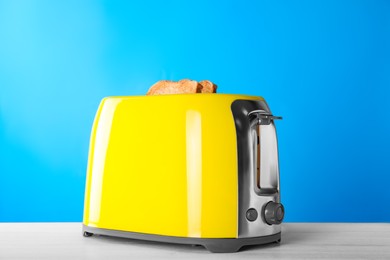 Modern toaster with slices of roasted bread on white wooden table