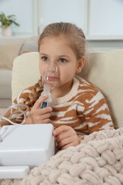 Photo of Little girl using nebulizer for inhalation in armchair at home