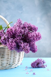 Photo of Beautiful lilac flowers in wicker basket on light blue wooden table