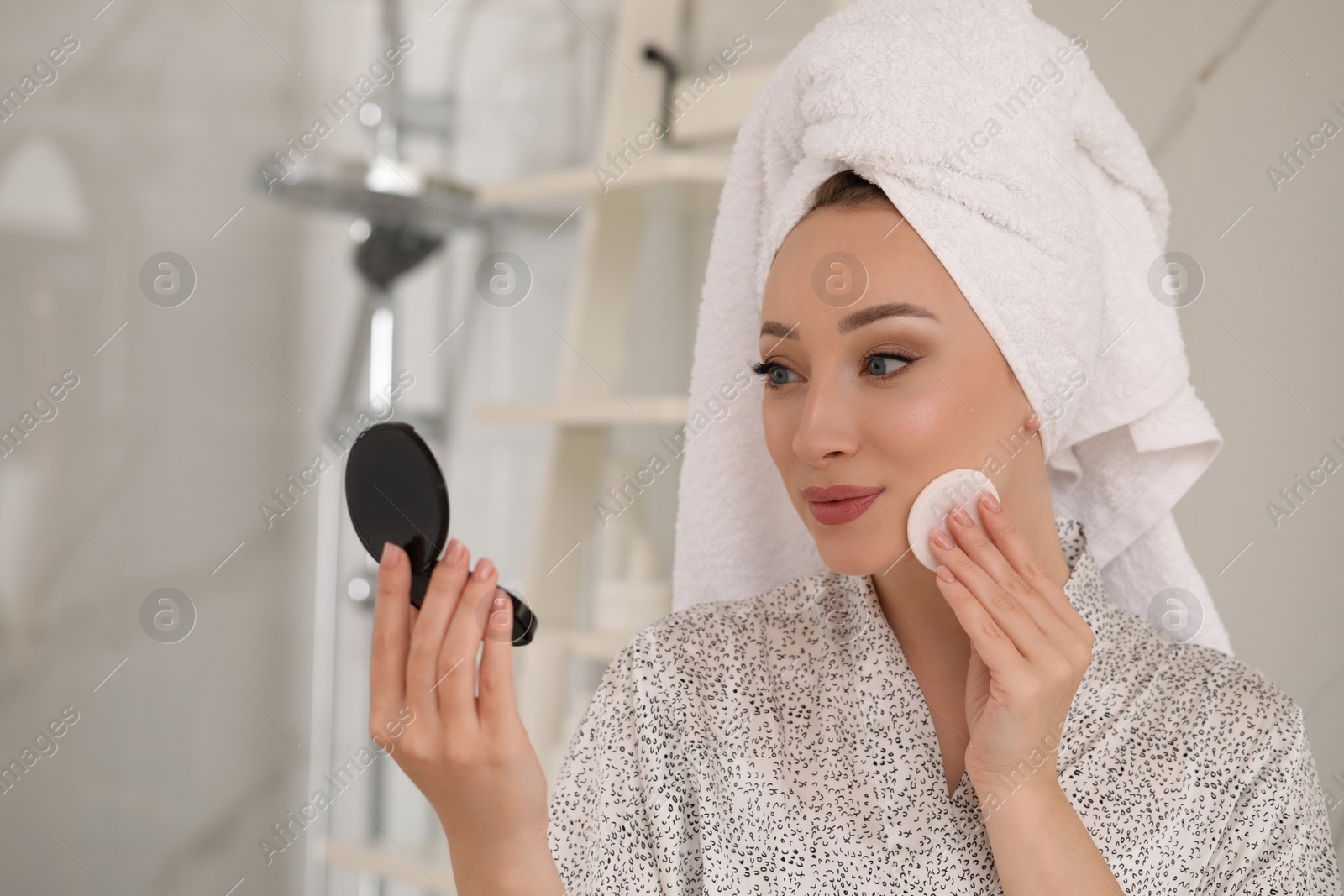 Photo of Beautiful young woman applying face powder with puff applicator in bathroom at home