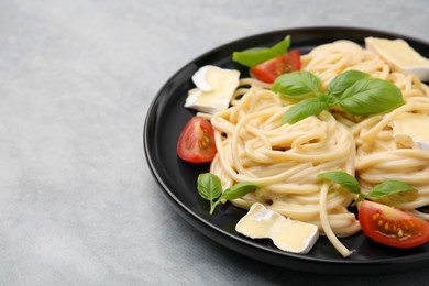 Photo of Delicious pasta with brie cheese, tomatoes and basil leaves on grey table, closeup. Space for text