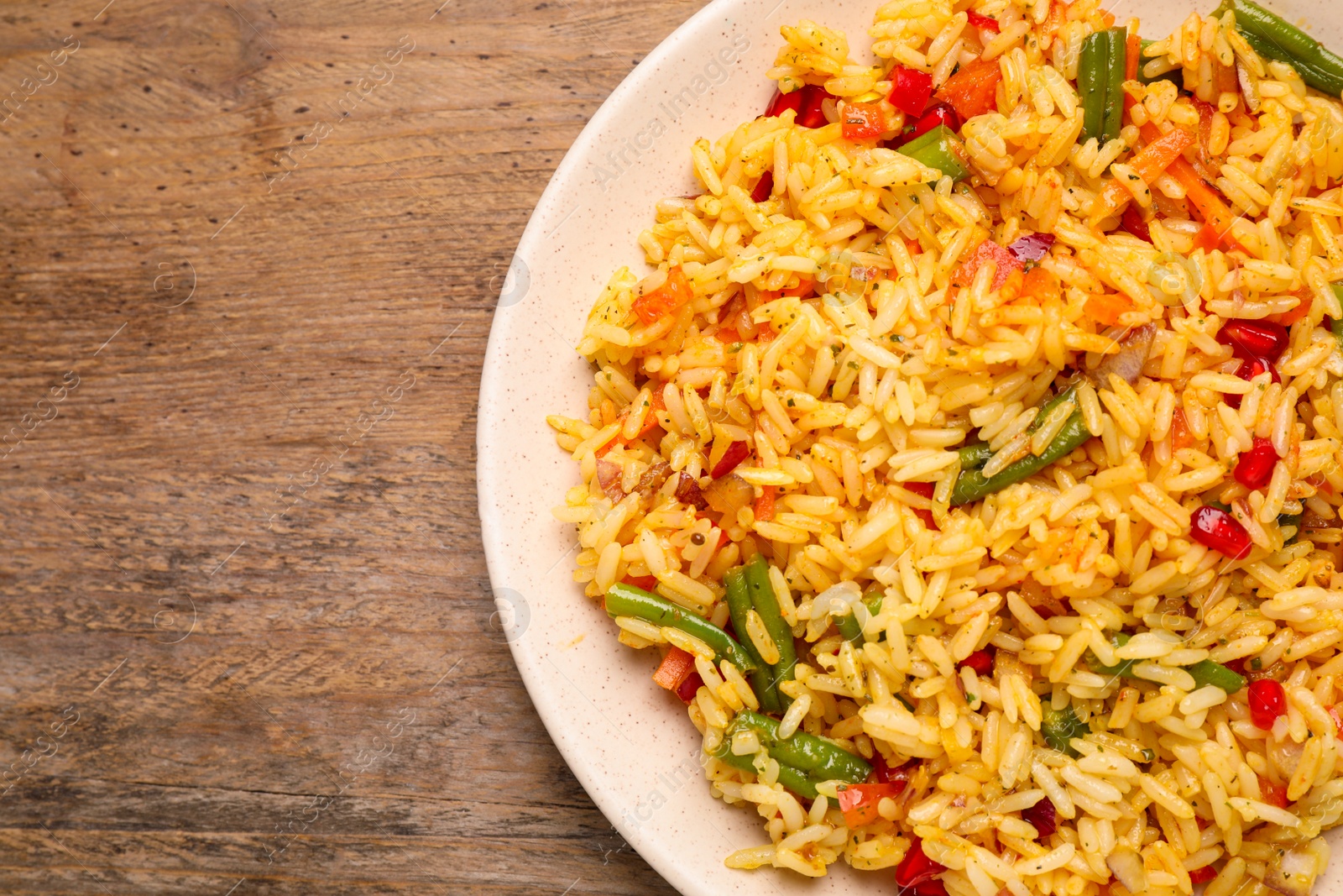 Photo of Tasty rice pilaf with vegetables on wooden table, top view