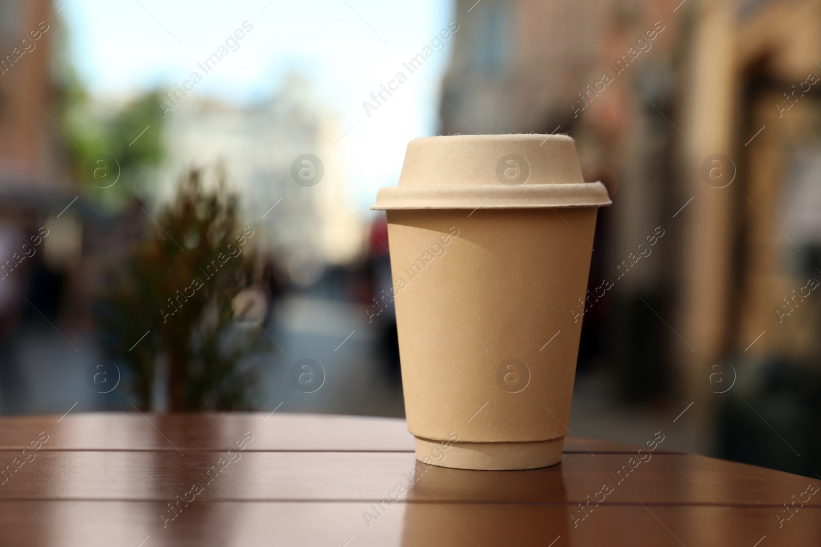 Photo of Cardboard takeaway coffee cup with lid on wooden table in city, space for text