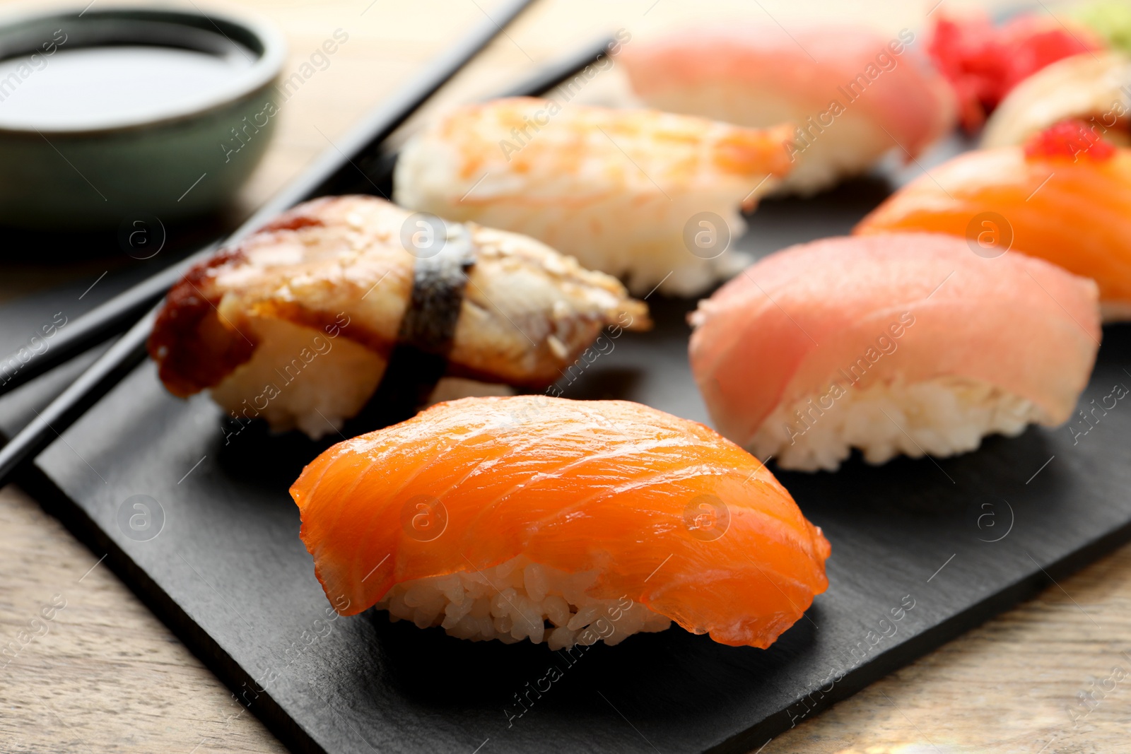 Photo of Serving board with delicious nigiri sushi and soy sauce on wooden table, closeup