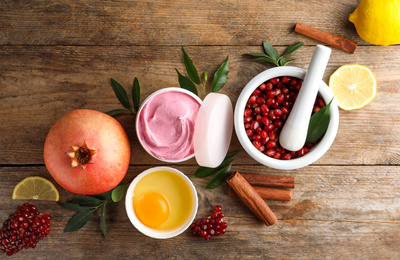 Photo of Flat lay composition with natural homemade mask, pomegranate and ingredients on wooden table