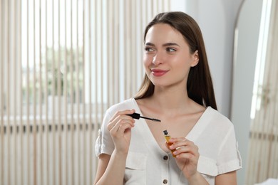 Photo of Young woman with eyelash oil at home, space for text