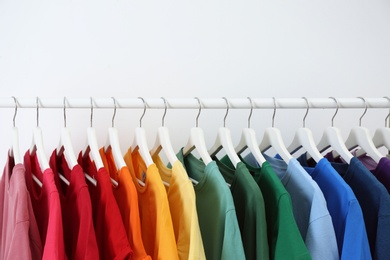 Photo of Rack with bright clothes on white background. Rainbow colors