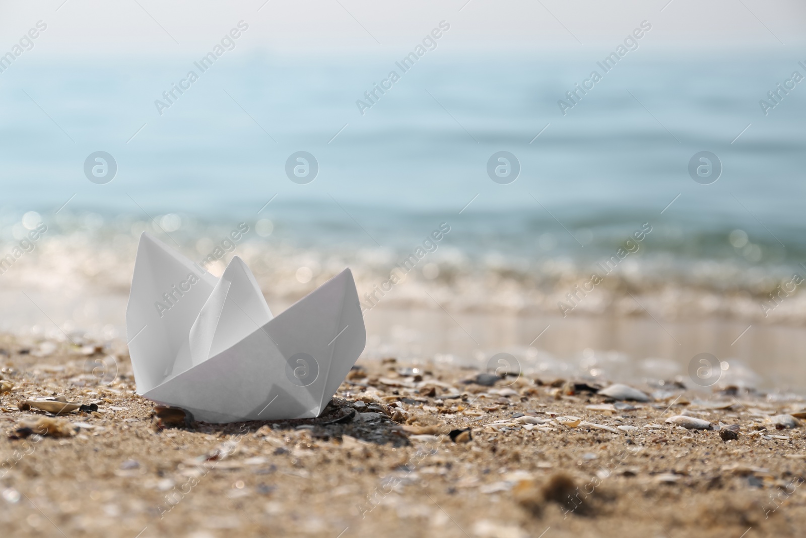 Photo of White paper boat on sandy beach near sea, space for text