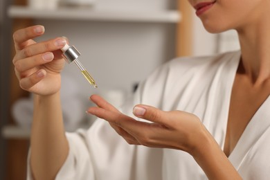 Photo of Woman applying cosmetic serum onto her hand in bathroom, closeup