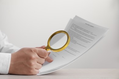 Photo of Man looking at document through magnifier at white wooden table, closeup. Searching concept