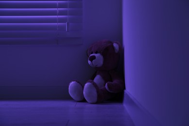 Cute lonely teddy bear on floor in corner of dark room