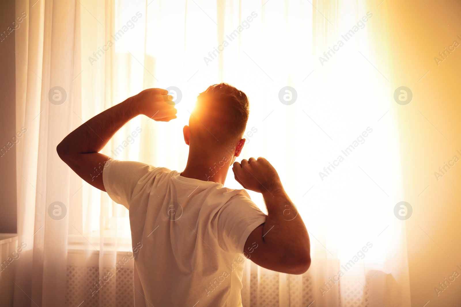 Photo of Man stretching near window at home, view from back. Lazy morning